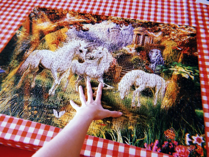 A photo of a finished unicorn puzzle. A hand is placed on top of it, lovingly.