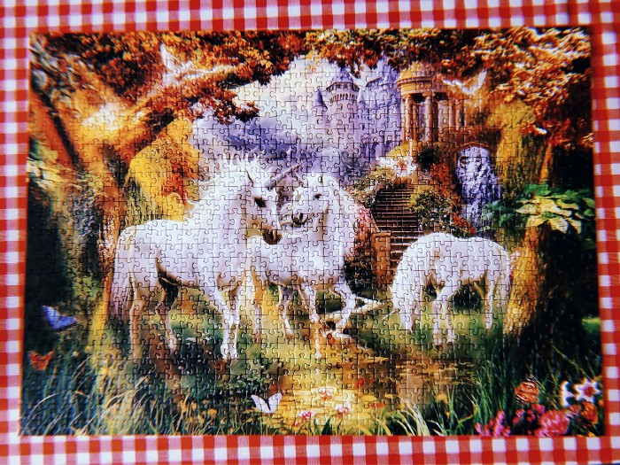 A completed puzzle of a three white unicorns in an idyllic woodland scene, seen from above.